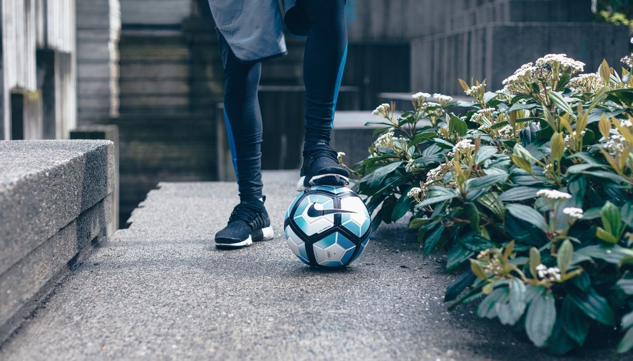 A male athlete in sportswear with a soccer ball in an urban outdoor setting.